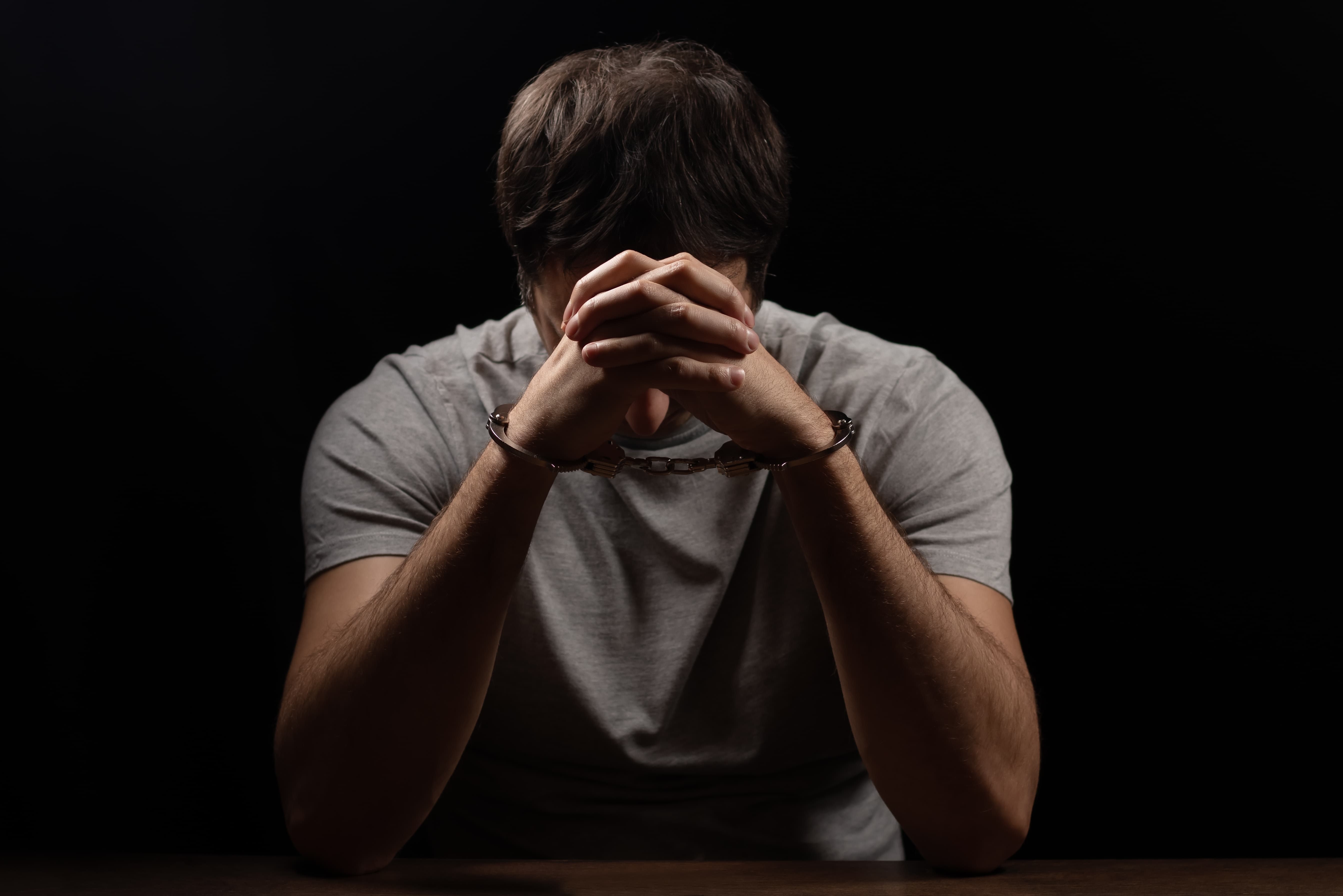 Handcuffed man covering his face with his hands
