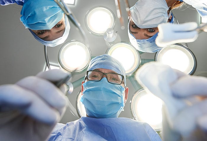 A group of medical professionals looking down on a patient, the image is viewed on the patients perspective.