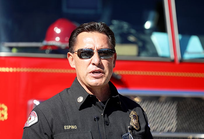 A picture of a fireman with glasses, in front of a firetruck.