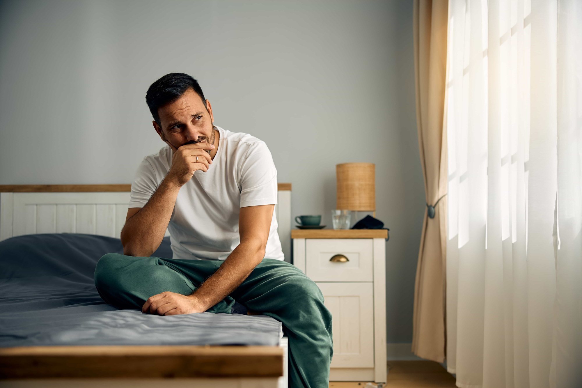 worried-man-sitting-in-his-bed-looking-out-the-window